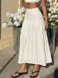 Person wearing a white pleated skirt with a blurred background of flowers and a building.