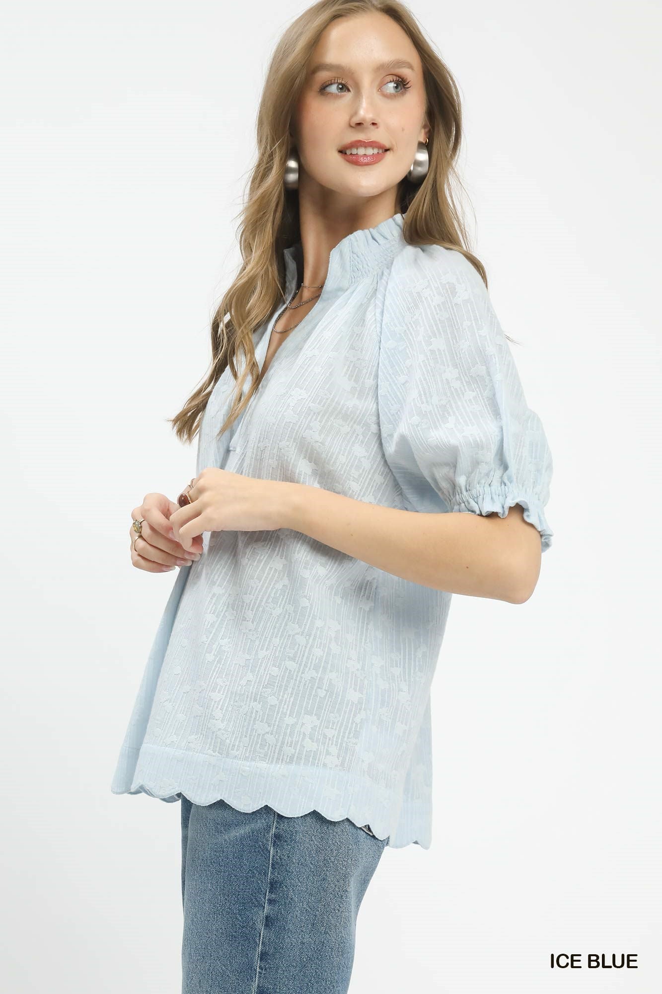 Woman wearing an ice blue blouse with scalloped hem on a white background