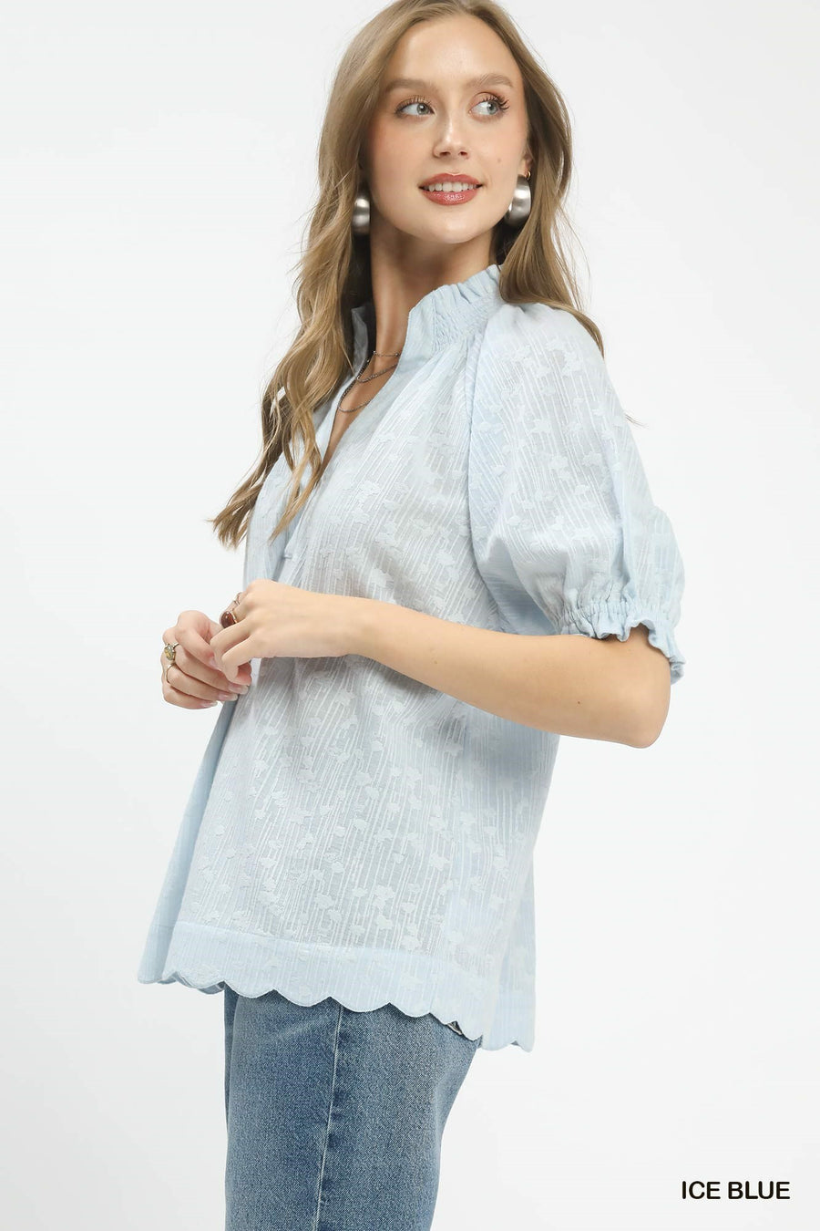 Woman wearing an ice blue blouse with scalloped hem on a white background