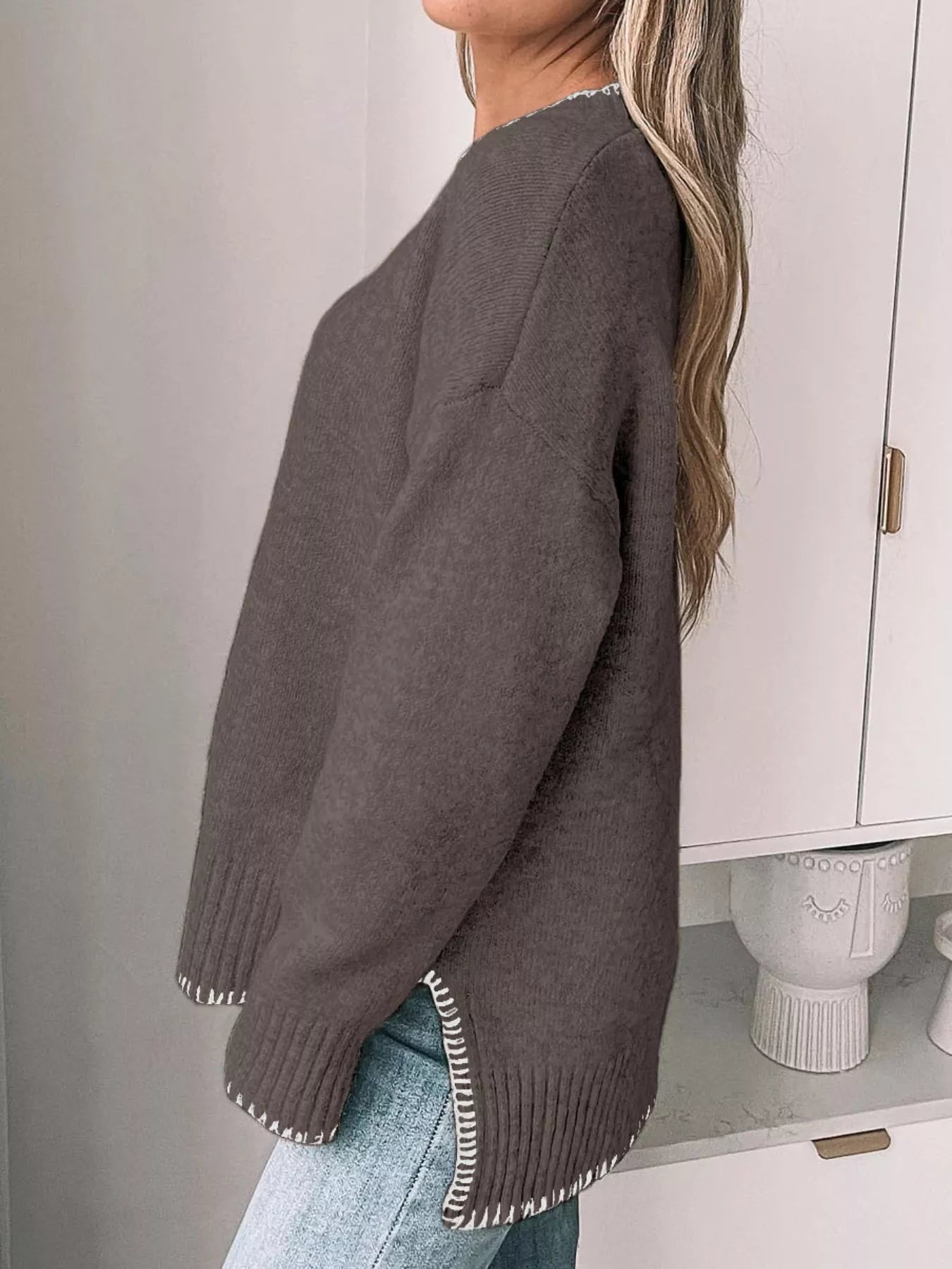 Person wearing a brown sweater with white trim in a minimal indoor setting