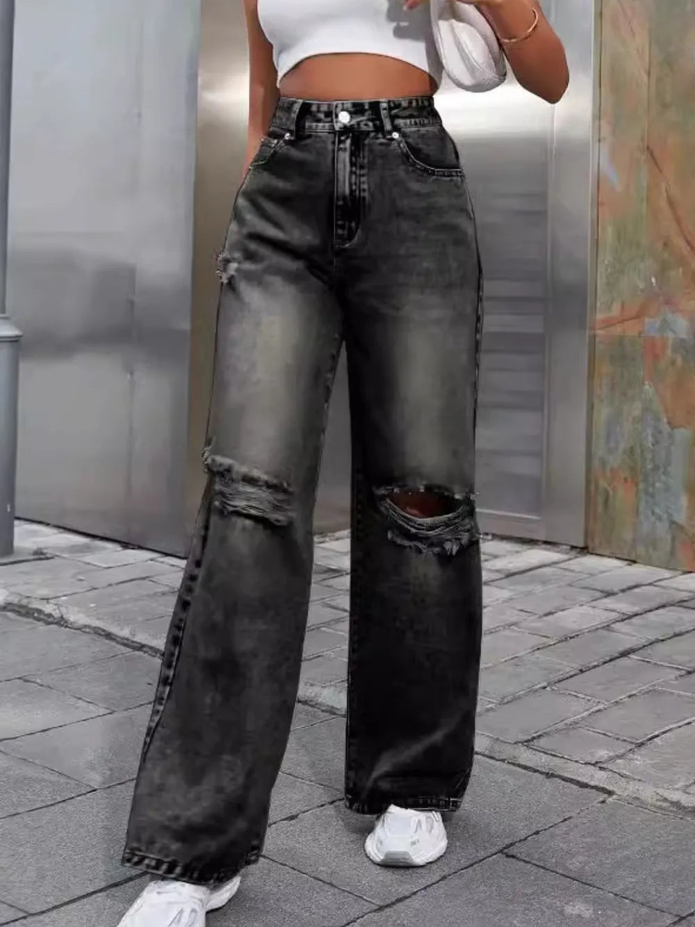 Person wearing high-waisted, distressed black jeans on a city street.