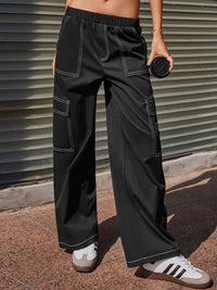 Person wearing black wide-leg pants with white stitching against a metallic background