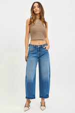 Woman wearing a beige top and blue jeans on a white background