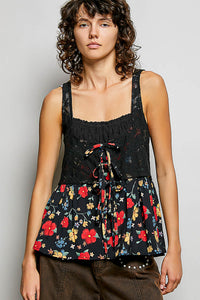 Woman wearing a black floral sleeveless top against a plain background
