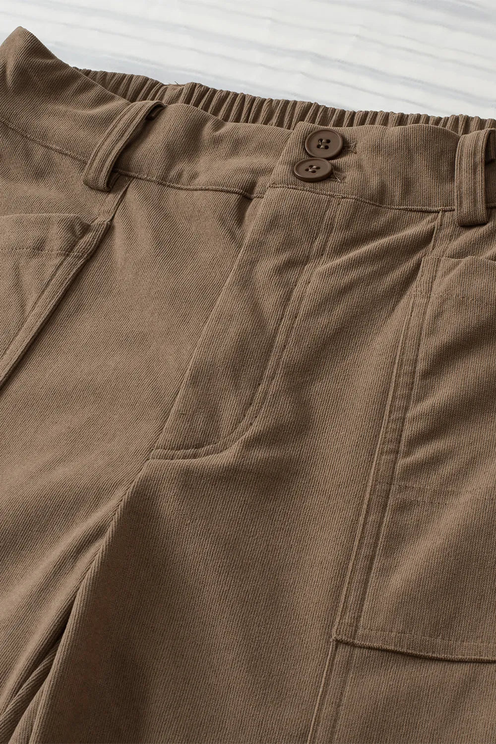 Close-up of brown pants with a button on a striped background