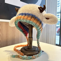 Colorful knitted hat with animal ears on a wooden stand indoors.