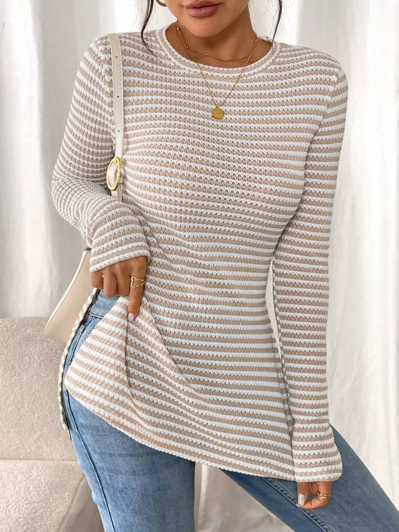 Person wearing a patterned long-sleeve top and jeans against a neutral background