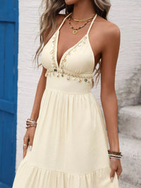 Woman wearing a beige halter neck dress with a white wall and blue door in the background