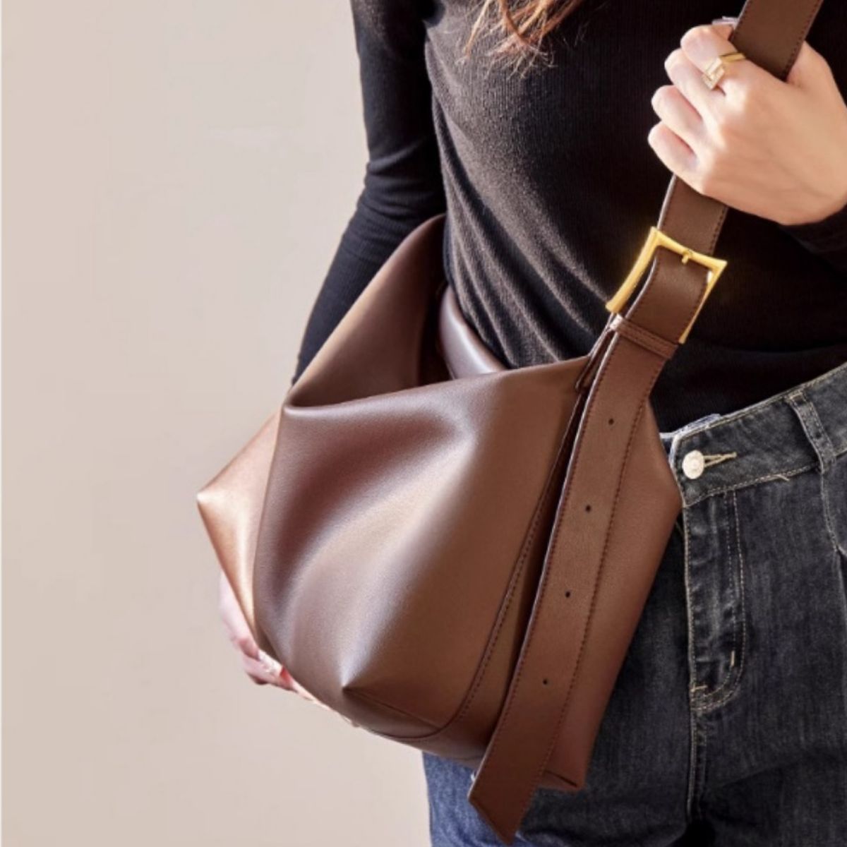 Brown leather bag being held by a person wearing a black top and blue jeans.
