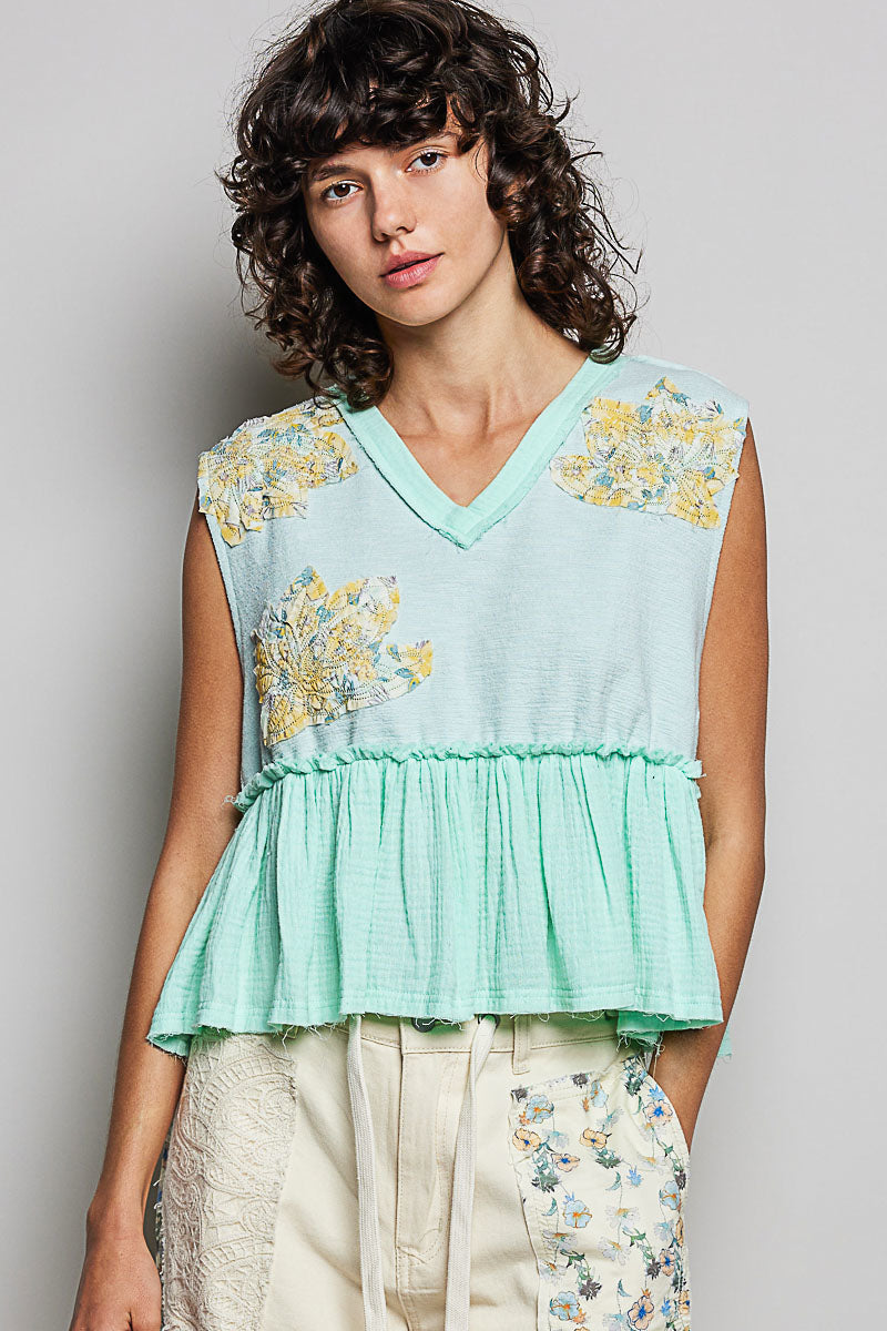 Woman wearing a light blue sleeveless top with floral patterns against a plain background