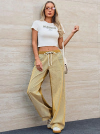 Woman wearing a white crop top and yellow pants against a beige wall.