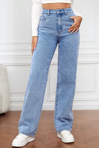 Person wearing light blue jeans and white sneakers on a wooden floor.