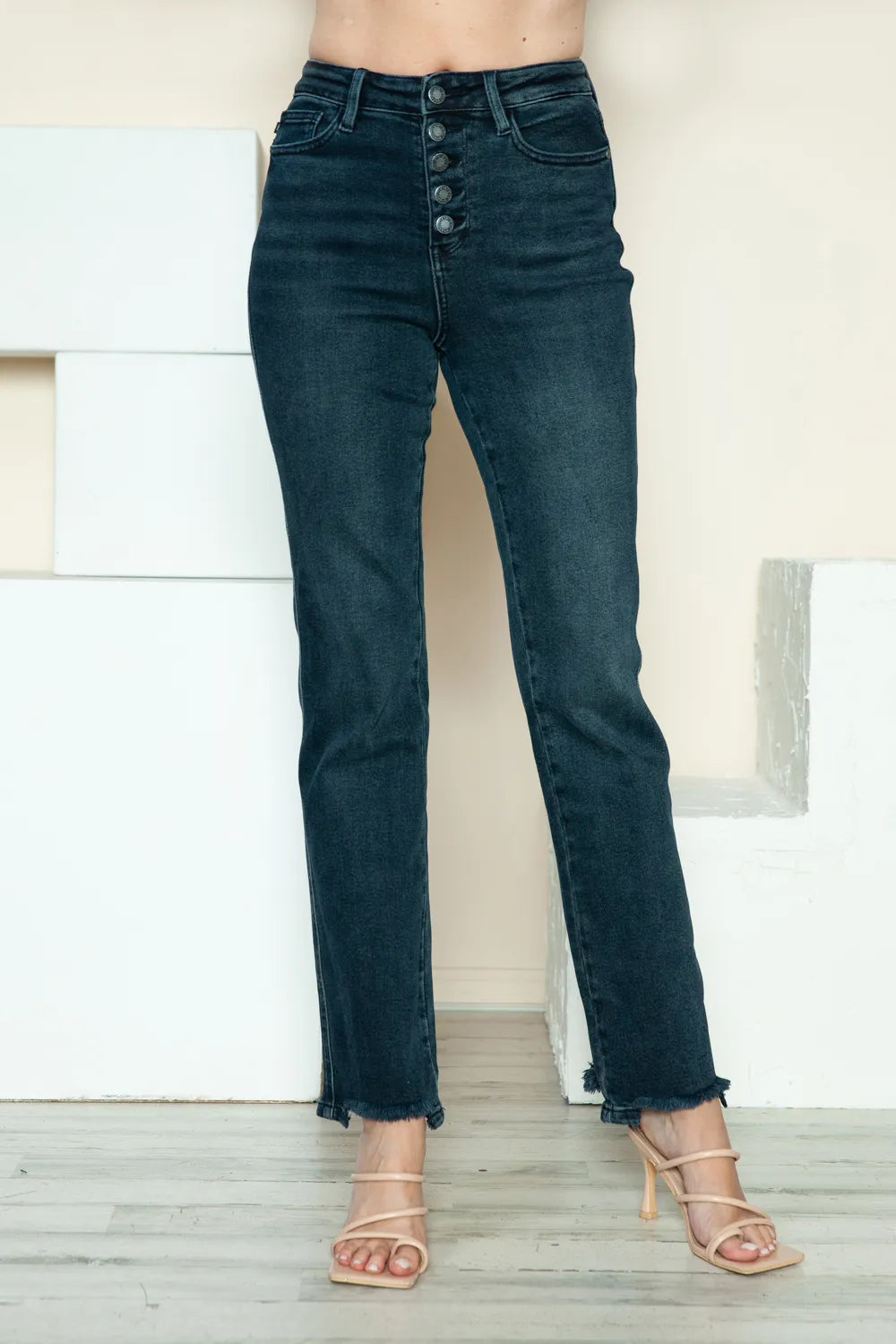 Black jeans worn by a person on a light wooden floor with a white wall background