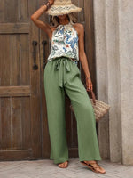 Woman wearing a floral top and green pants standing in front of a wooden door.