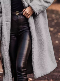 Person wearing a long gray coat and black leather pants with a blurred background