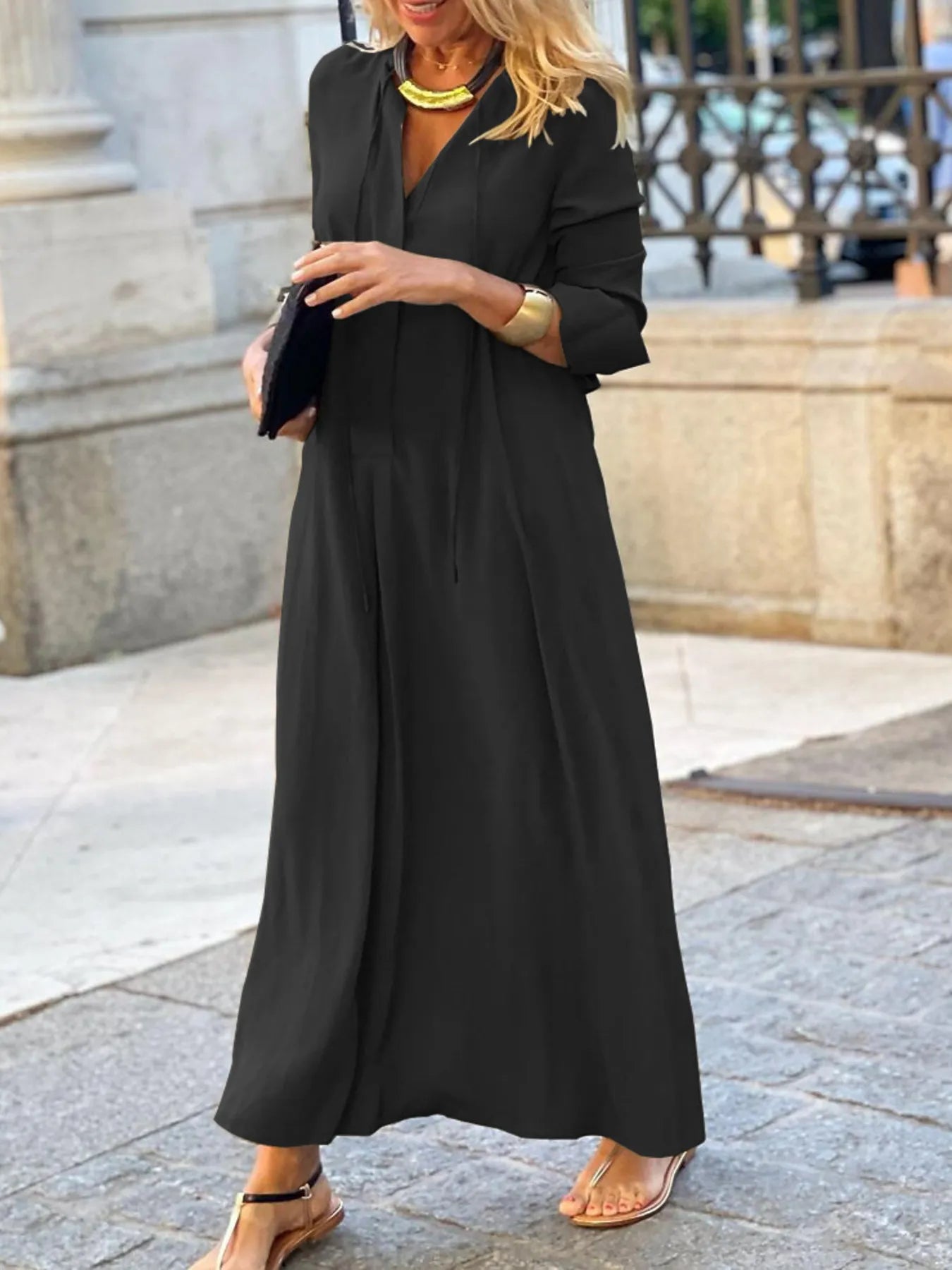 Woman wearing a long black dress standing on a stone pavement.