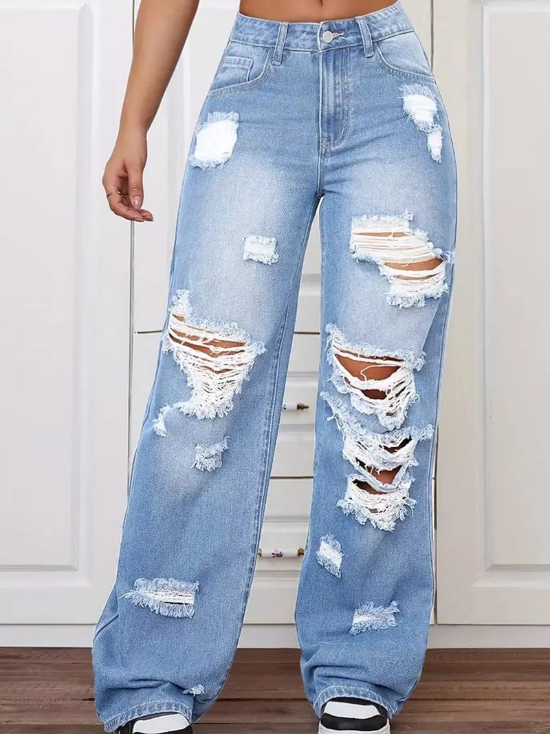 Light wash blue distressed wide-leg jeans with ripped details and frayed edges, shown on a model from the waist down against a white paneled wall.