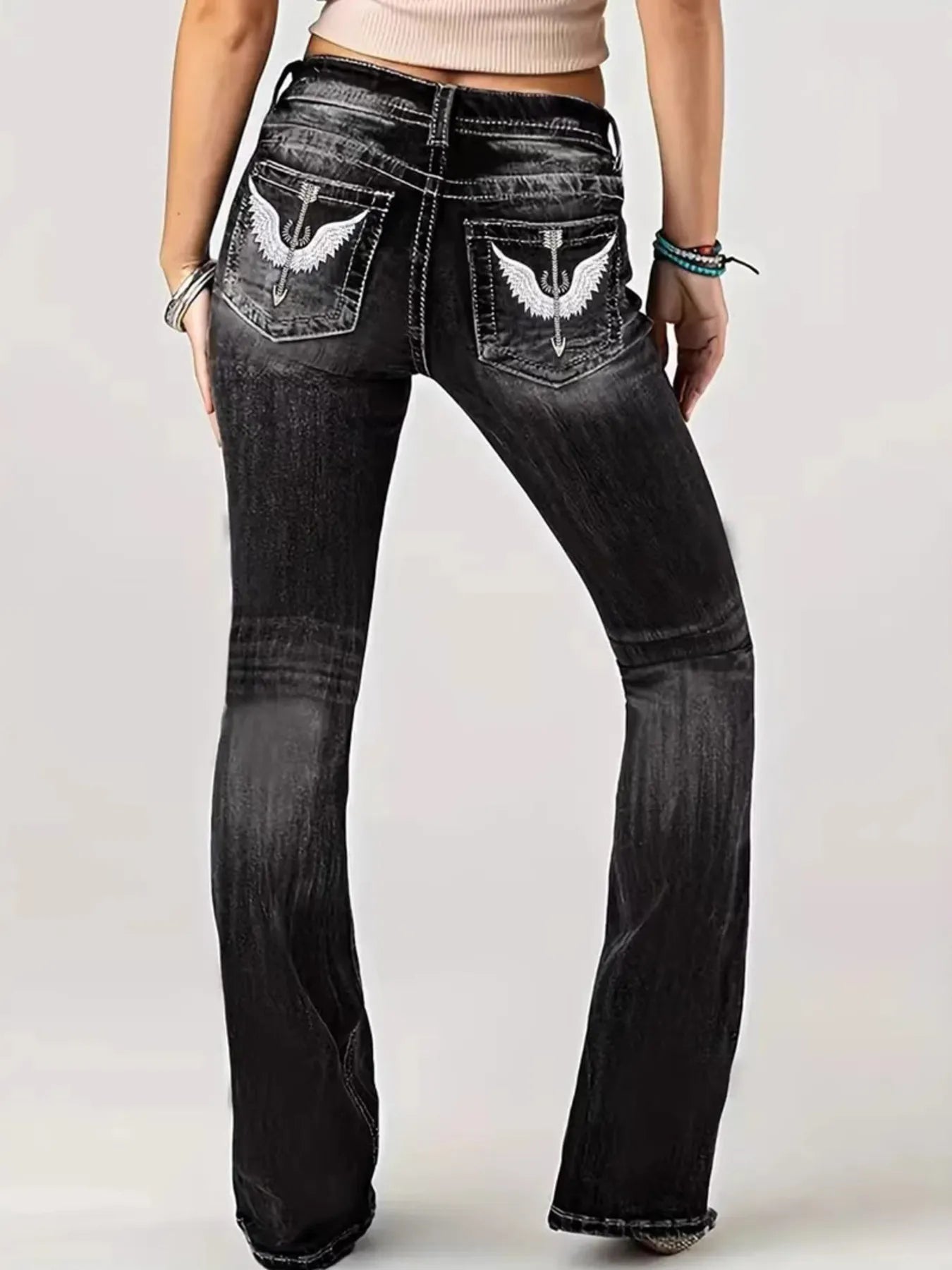 Black jeans with white eagle designs on the pockets against a white background