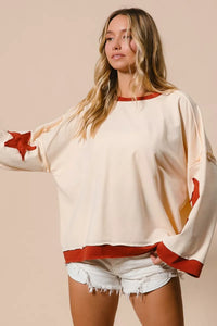 Woman wearing a cream sweater with red accents and denim shorts on a beige background