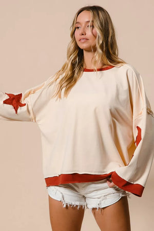 Woman wearing a cream sweater with red accents and denim shorts on a beige background