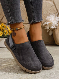 Dark gray slip-on shoes worn with jeans on a neutral background