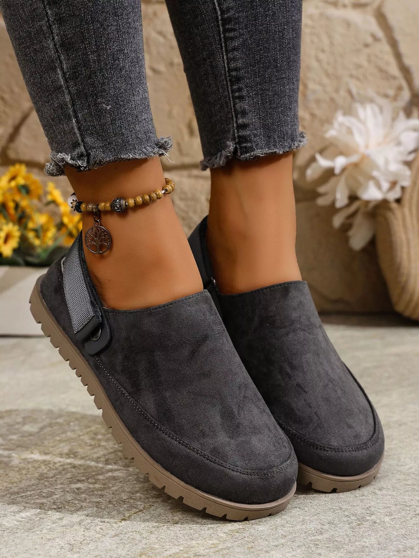 Dark gray slip-on shoes worn with jeans on a neutral background