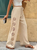 Person wearing beige pants with floral cutouts against a textured wall.