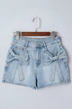 Light blue denim shorts with bow details on a hanger against a white background