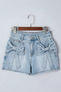Light blue denim shorts with bow details on a hanger against a white background
