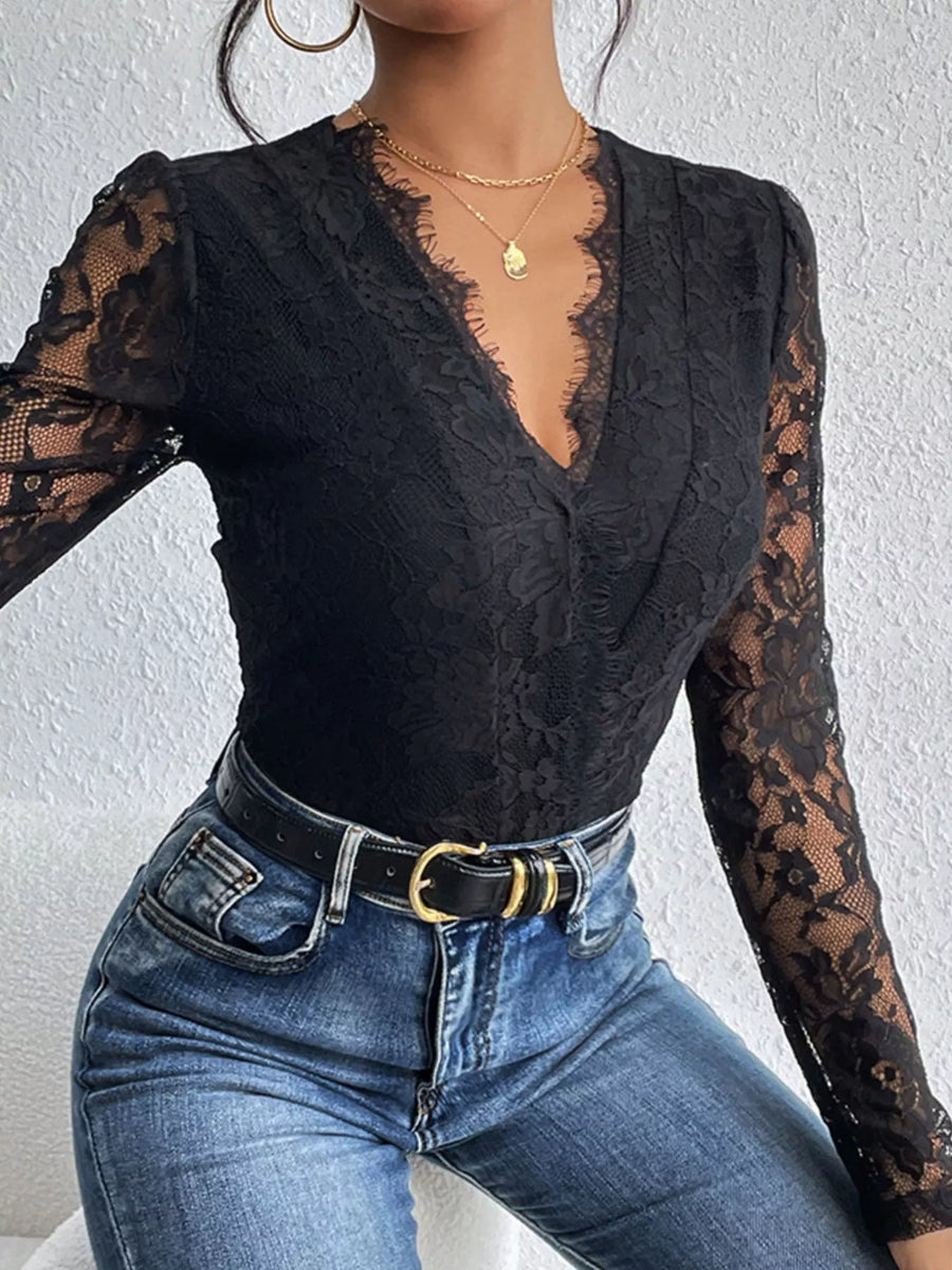 Person wearing a black lace long-sleeve top and blue jeans against a white background