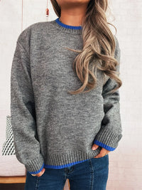 Person wearing a gray sweater with blue trim against a neutral background