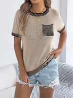 Woman wearing a beige short-sleeve top with black trim and denim shorts on a white background
