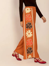 Person wearing a long, patterned orange skirt with floral designs on a beige background