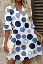 Woman wearing a white dress with blue polka dot pattern, holding a white clutch.