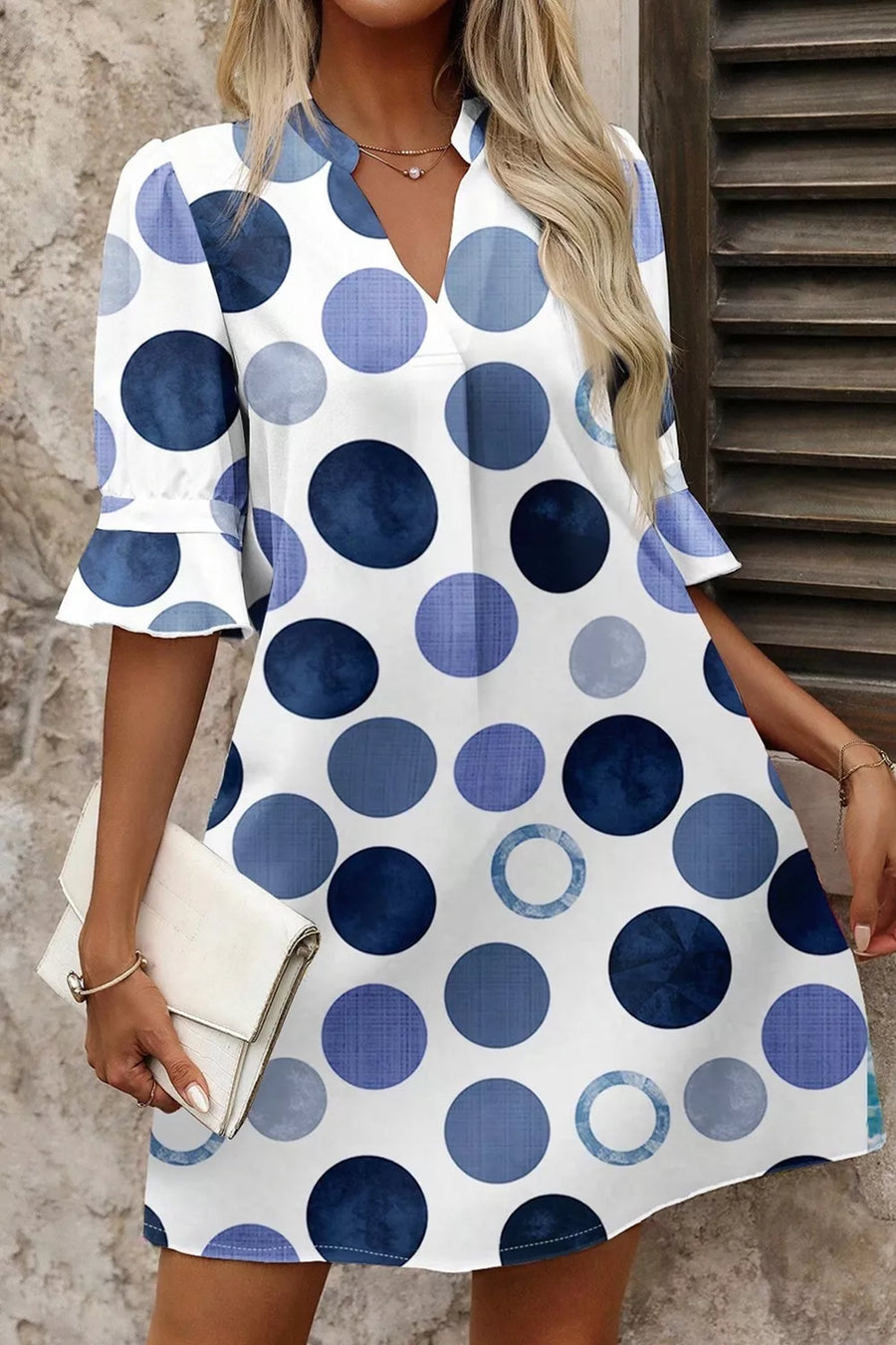Woman wearing a white dress with blue polka dot pattern, holding a white clutch.