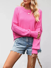 Person wearing a pink sweater and denim shorts on a plain background