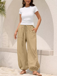 Woman wearing a white t-shirt and beige wide-leg pants standing against a light-colored wall.