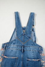 Blue denim overalls with floral patterns on a white background