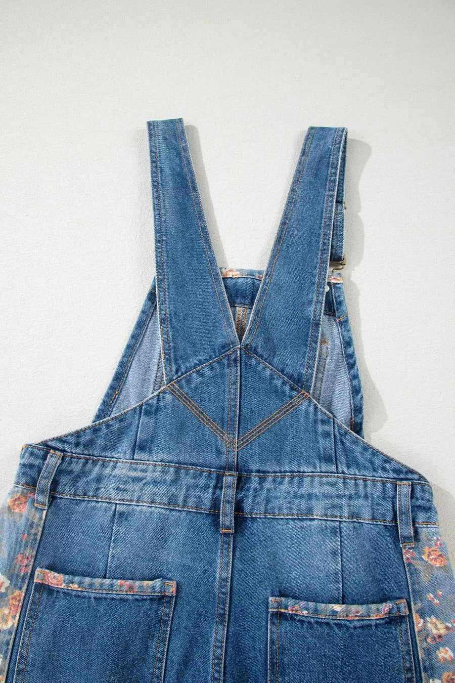 Blue denim overalls with floral patterns on a white background
