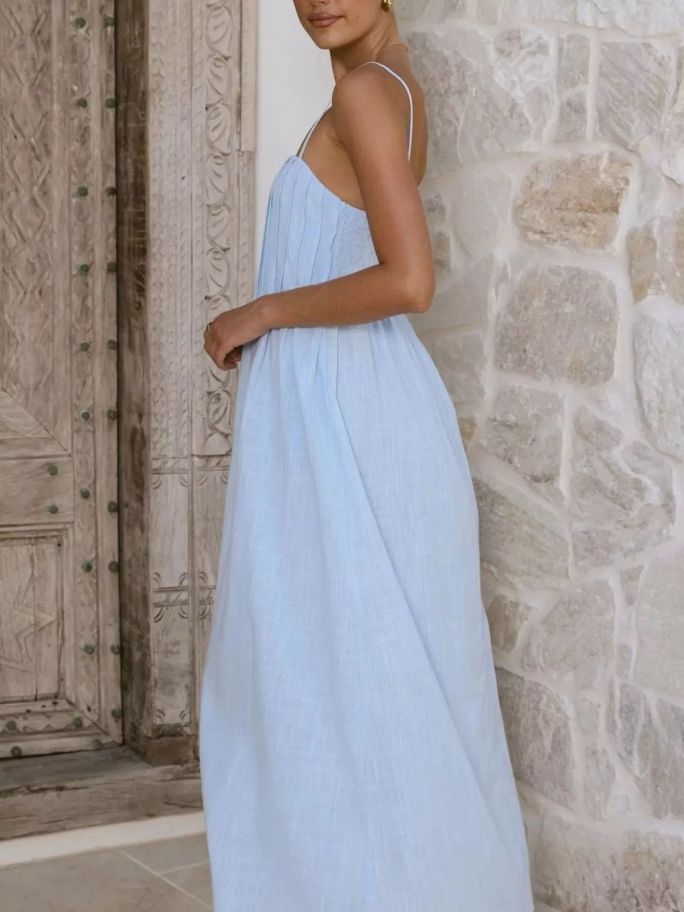 Woman wearing a light blue dress standing against a stone wall.