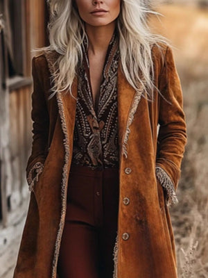 Person wearing a long brown coat with intricate patterns, standing outdoors.