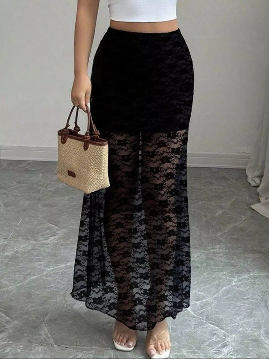 Person wearing a black lace skirt holding a straw bag on a gray floor.