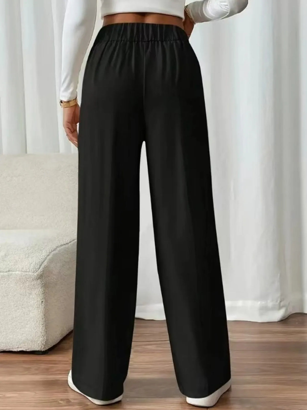 Person wearing black wide-leg pants with a white top and shoes in a minimal indoor setting.