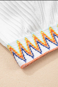Close-up of a white fabric with colorful embroidered pattern on a beige surface