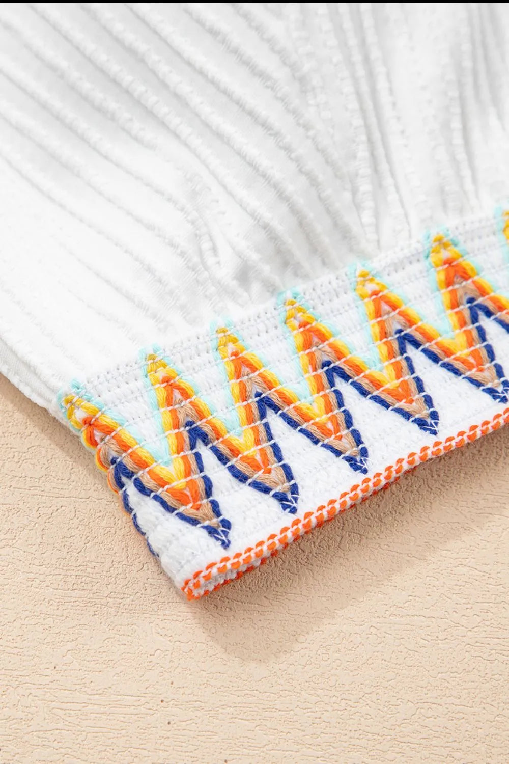 Close-up of a white fabric with colorful embroidered pattern on a beige surface