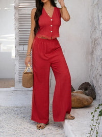 Woman wearing a red outfit with wide-leg pants and a sleeveless top, standing against a white wall.