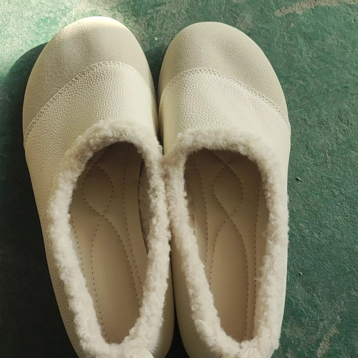 Pair of beige slippers with fuzzy lining on a green surface