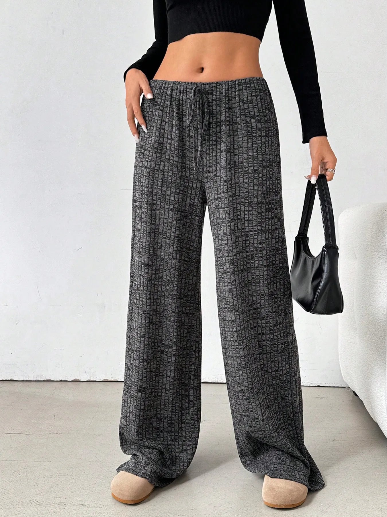 Person wearing wide-leg checkered pants holding a black handbag against a white background