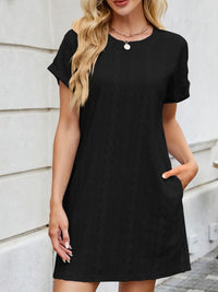Woman wearing a black dress against a light-colored wall.