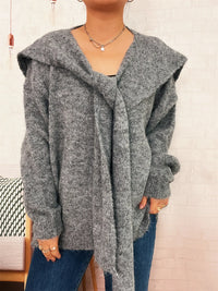 Person wearing a gray hooded cardigan with a neutral background